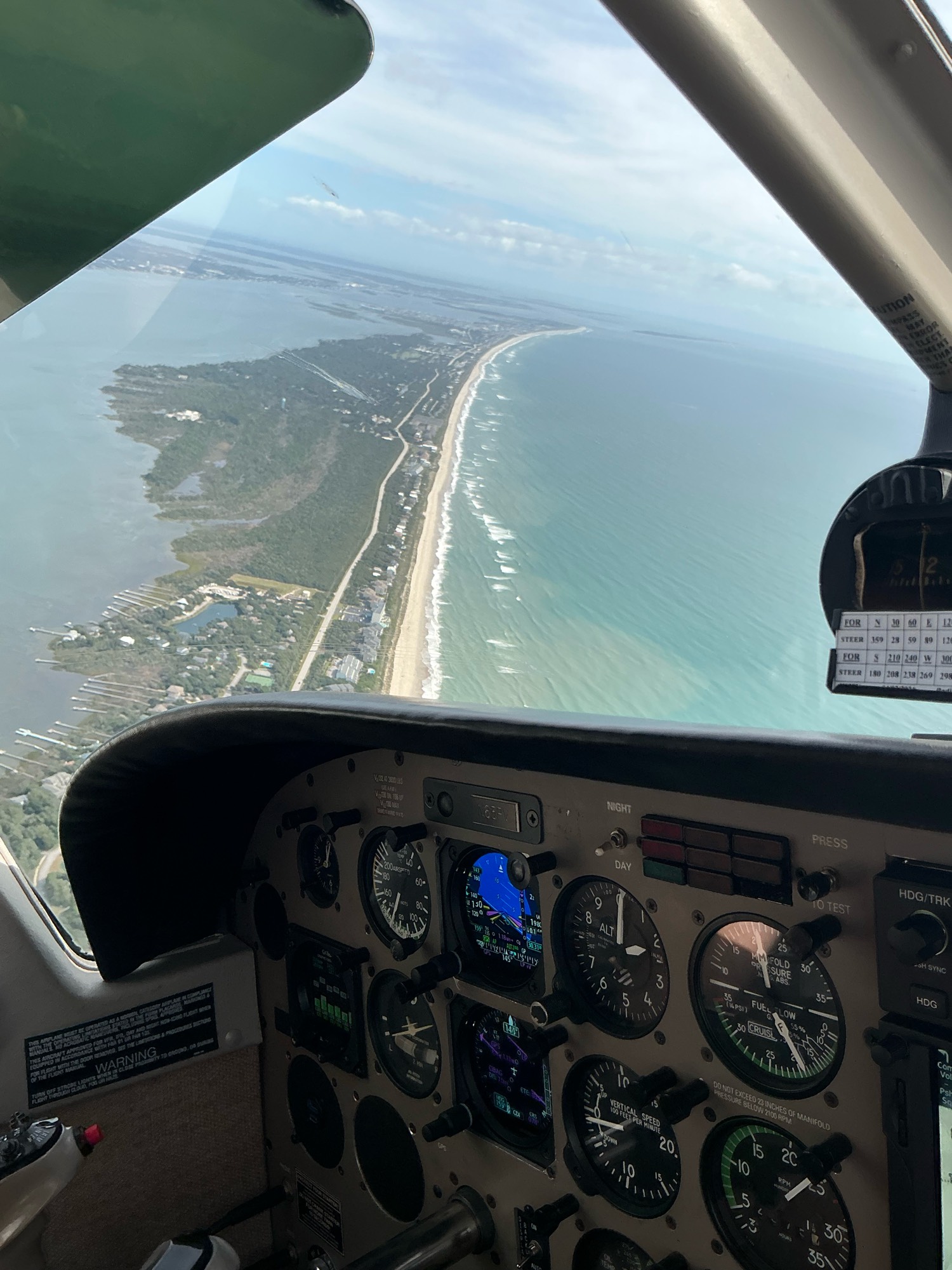 A barrier-island coastline through the windscreen of the club's Saratoga in flight